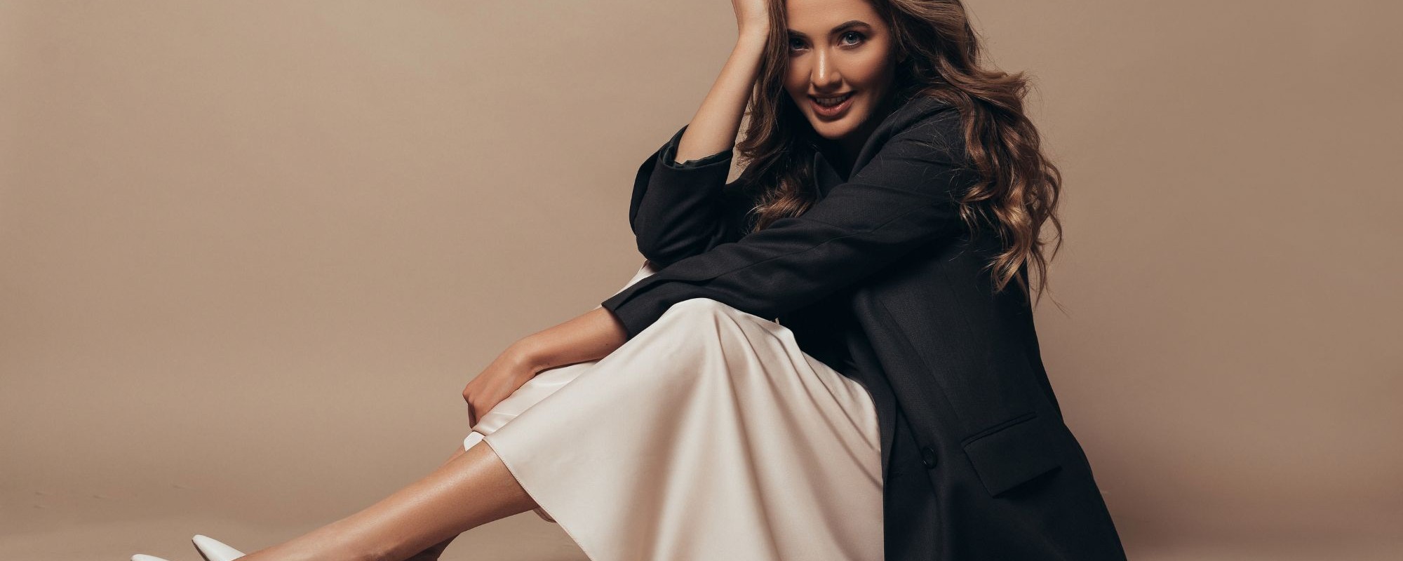 cheerful-model-sitting-floor-wearing-modern-oversize-black-jacket-creamy-long-dress-high-heel-shoes-her-feet-curly-hairstyle-makeup