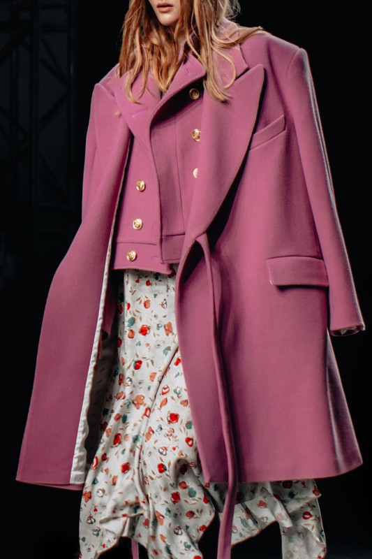 przycieta-postac-kobieca-ubrana-w-klasyczny-dlugi-rozowy-fantazyjny-plaszcz-i-biala-spodnice-spacerujaca-po-wybiegu