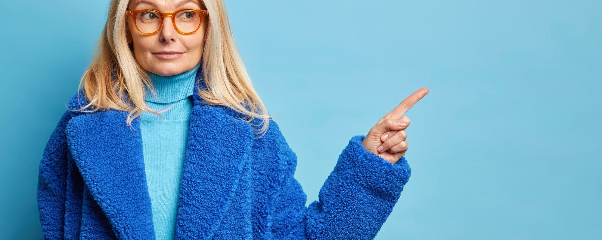serious-blonde-forty-years-old-caucasian-woman-has-curious-expression-indicates-away-blank-space-wears-optical-glasses-stylish-fur-coat